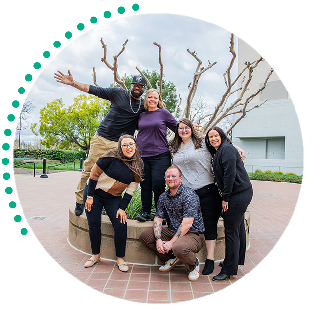 Group of people posing and smiling in front of office park greenery